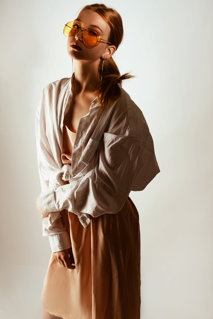 Home Trendy woman posing in oversized shirt and sunglasses, exuding modern fashion style.