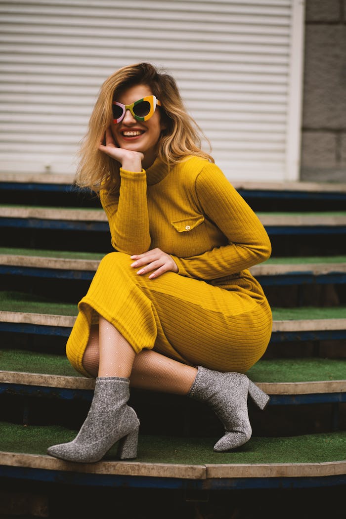 About Stylish woman in yellow dress and sunglasses posing on steps. Modern fashion portrait.